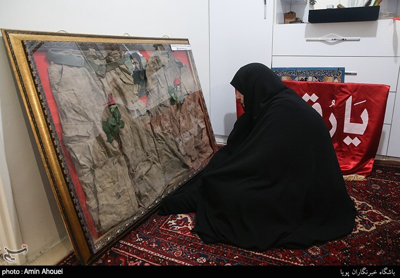 مادر شهید مدافع حرم جواد الله کرم در حال ادای احترام به لباس تفحص شده ی فرزندش